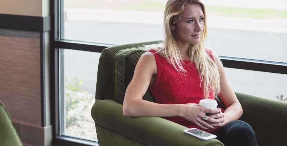 Photo of a girl who is sitting on a sofa with a cup of coffee.