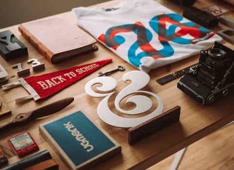 Old camera, shirt, notepad, red flag, old key. All neatly stacked on a wooden table.